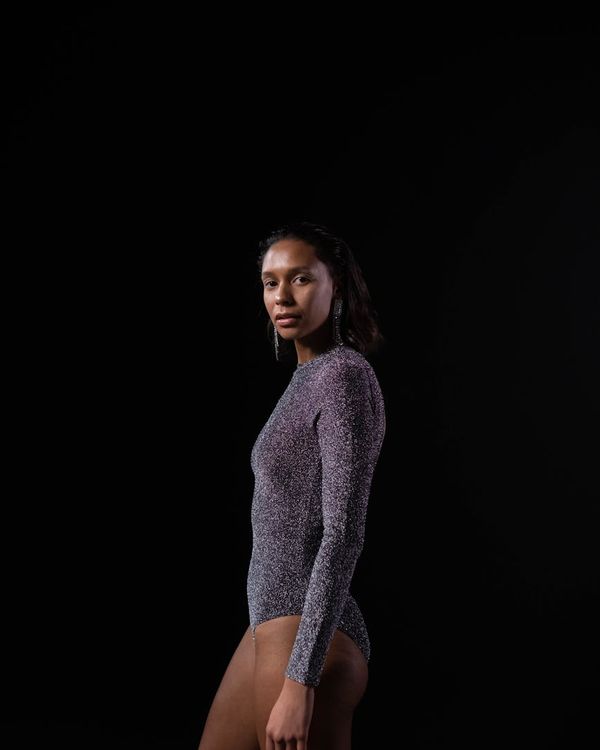 Woman in a calm yoga pose in a dark room with soft pink light.